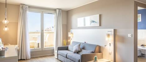 A modern living room with a grey sofa, a white side table, and a large window with curtains.