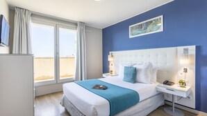 Een hotelkamer met een groot bed, een nachtkastje met een lamp, een telefoon en een kleine plant.