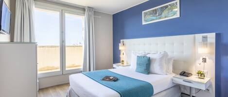 Habitación de hotel con una cama grande, una mesita de noche con lámpara, teléfono y una pequeña planta.