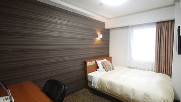 Une chambre d’hôtel comprenant un lit, un bureau avec un téléphone, une tête de lit, une lampe fixée au mur et une fenêtre avec des rideaux.