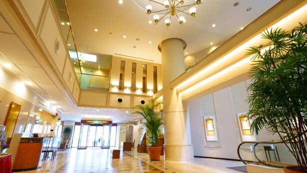 A spacious lobby with a high ceiling, a central chandelier, and a check-in desk.