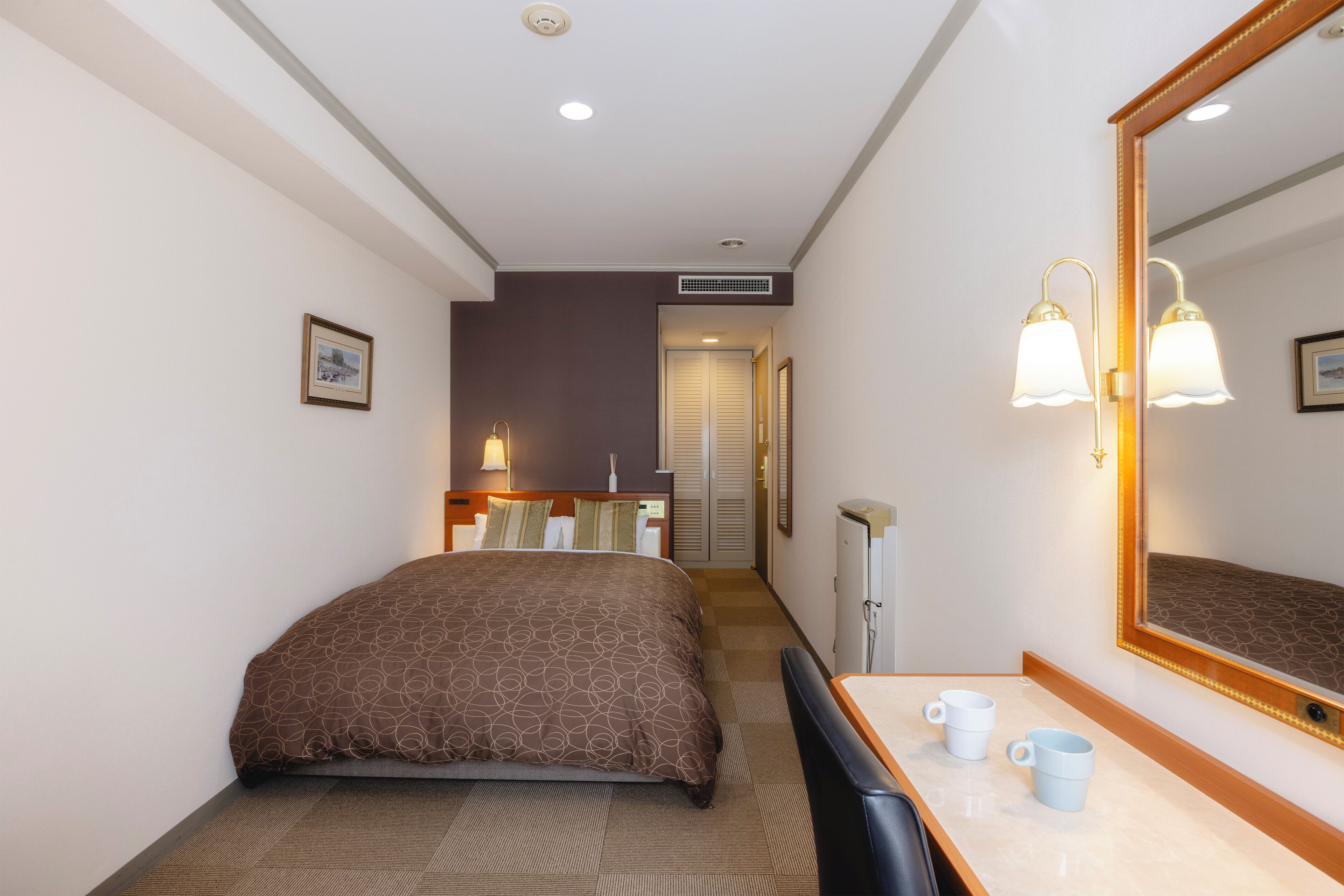 Une chambre d’hôtel comprenant un lit, une table de chevet, deux lampes de chevet, un miroir et une porte donnant accès à une salle de bain.