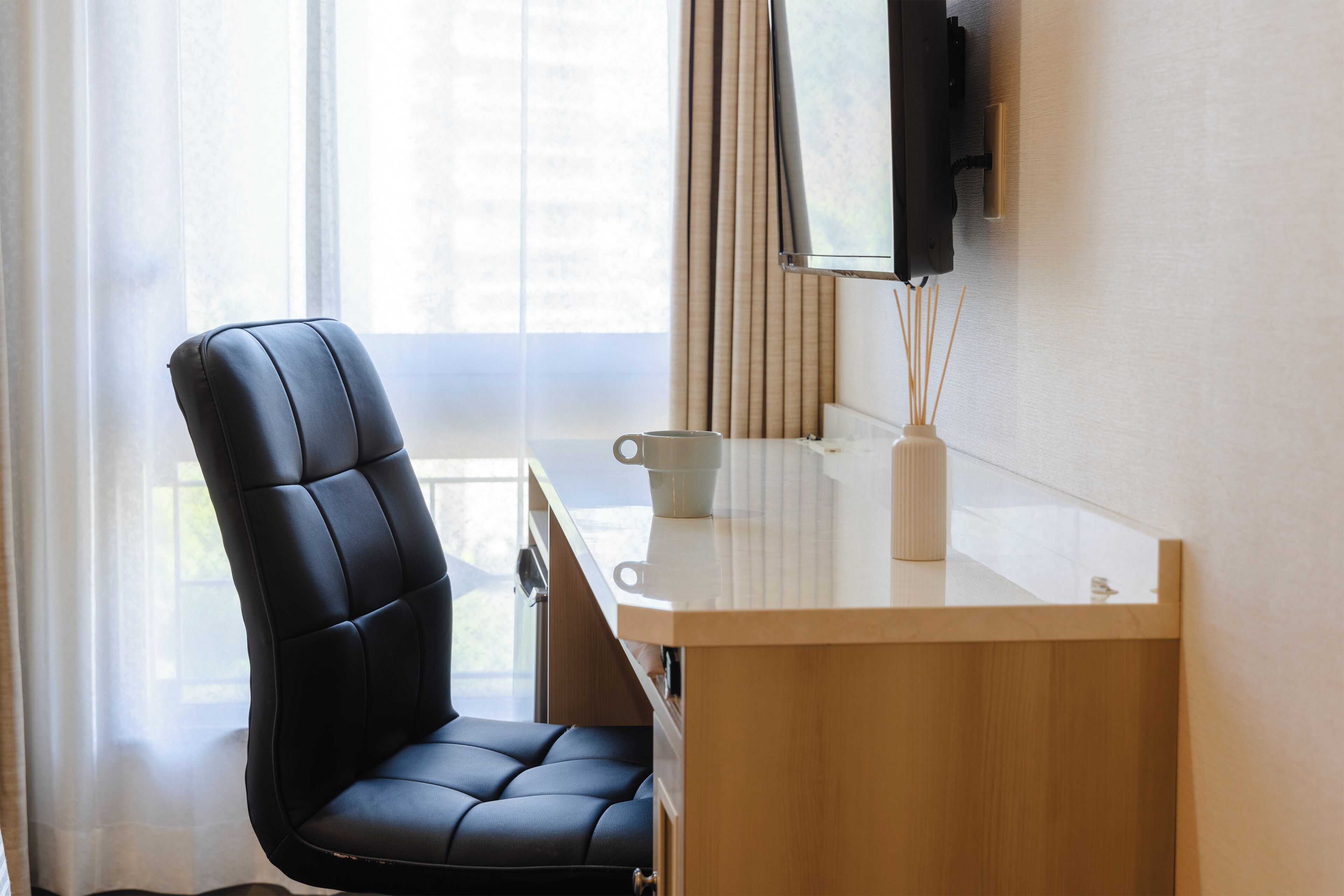 A modern office chair, a desk, a television mounted on the wall, and a window with curtains.
