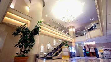 A spacious lobby with a high ceiling, a central staircase, and a reception desk.