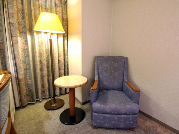 A corner room with a floral curtain, a round table with a lamp, and a blue armchair. - Sasebo Washington Hotel (Sasebo)