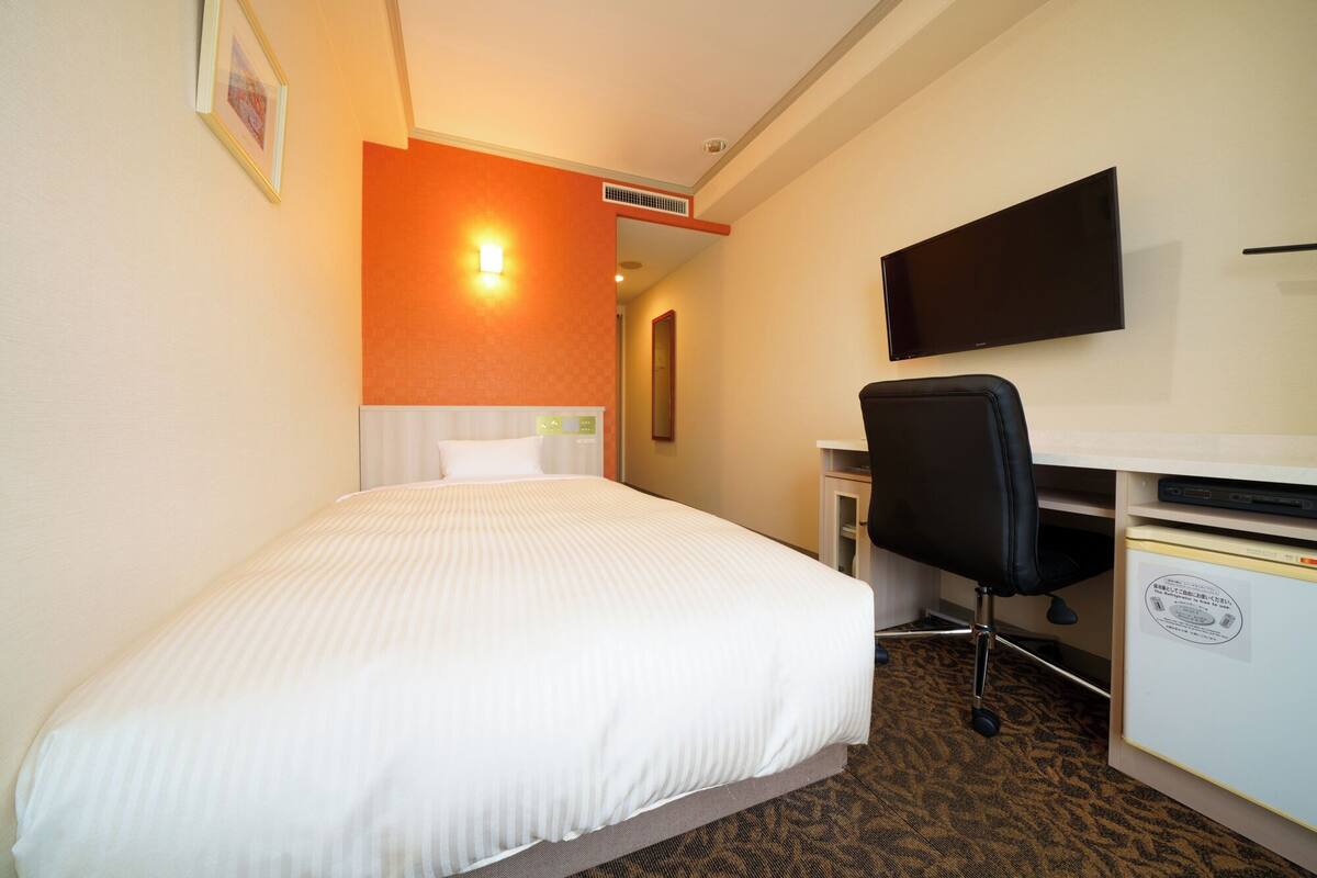 Habitación de hotel con cama, escritorio, silla, televisor de pantalla plana y luz empotrada en la pared.