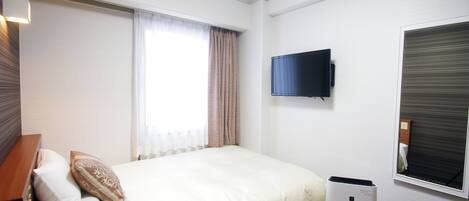 Habitación de hotel con cama, televisor de pantalla plana en la pared y ventana con cortinas.
