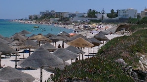 A beach with thatched umbrellas, a sandy shore, and buildings in the background. - The Dunes Golf & Spa Resort (Port El Kantaoui)