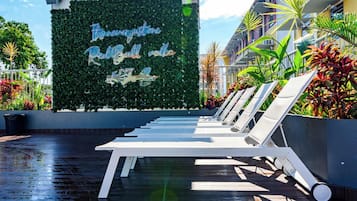 A pool area with lounge chairs and a wall with greenery and text.