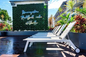 Un espace piscine avec des chaises longues et un mur agrémenté de plantes et d’une inscription.