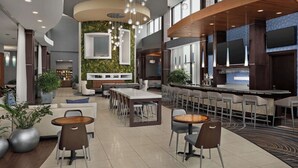 Un moderno vestíbulo de hotel con zona de bar, arreglos de asientos y una planta grande.