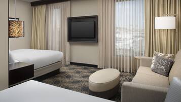 Ein Hotelzimmer mit einem Bett, einem Sofa, einem Fernseher und einem Fenster mit Vorhängen.