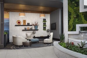A modern living room with a fireplace, seating, and a view of a green wall. - Embassy Suites by Hilton Knoxville West (Knoxville)
