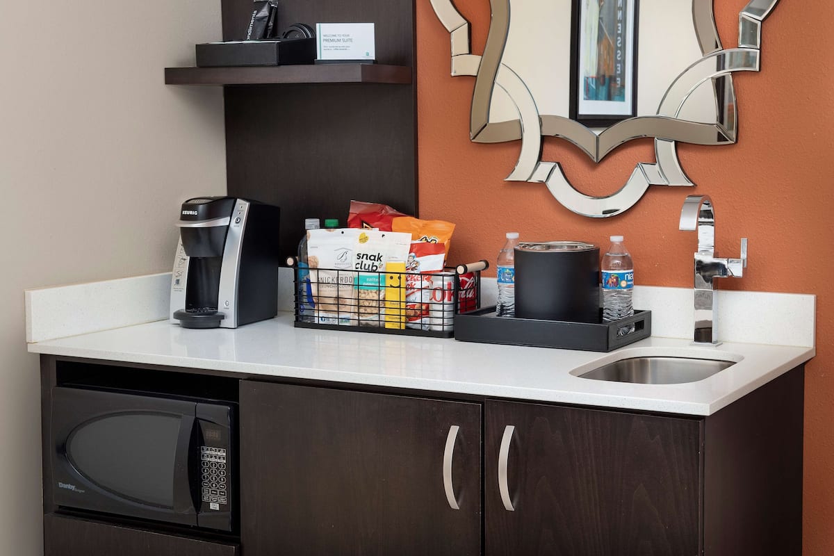 A hotel kitchenette with a coffee maker, microwave, and a snack basket.