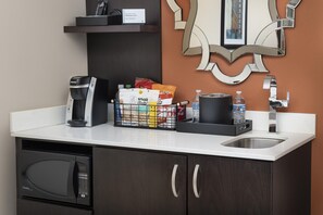 Una kitchenette con cafetera, cesta de snacks, botella de agua y microondas.