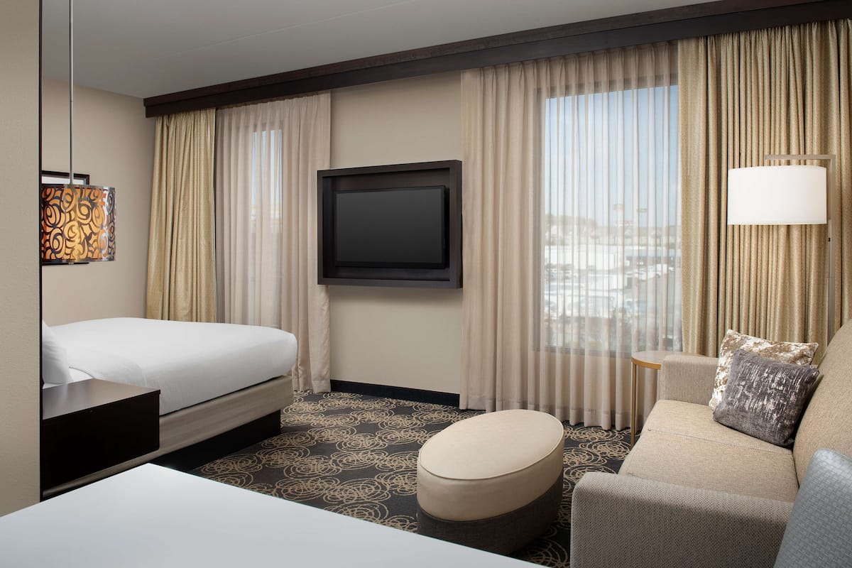 A hotel room with a bed, a sofa, a TV, and a lamp.