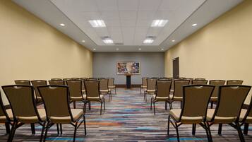A conference room with rows of chairs, a carpeted floor, and a painting on the wall.