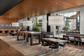 Un lobby moderno de hotel con una zona de bar, diferentes arreglos de asientos y grandes ventanales.