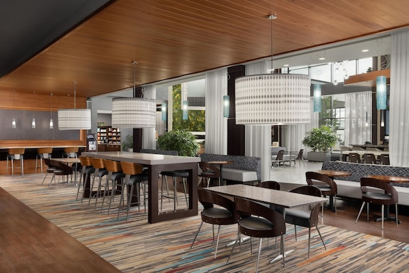 A modern hotel lobby with a bar area, seating arrangements, and large windows.