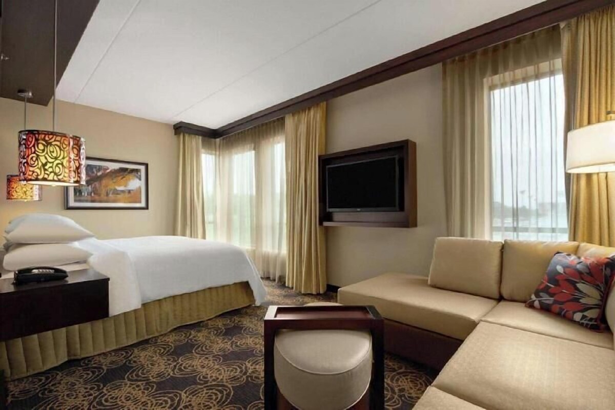 A hotel room with a bed, a sofa, a TV, and a desk with a lamp.