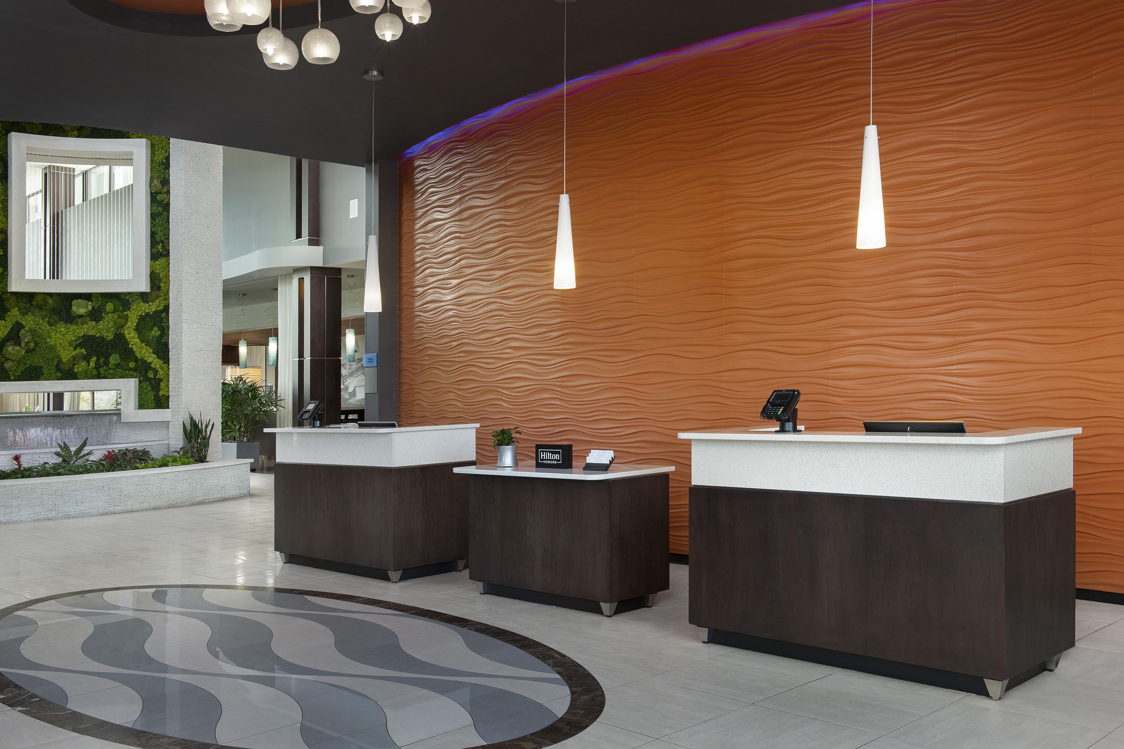 Zona de recepción de hotel con tres mostradores, diseño moderno y una alfombra grande y curvada.