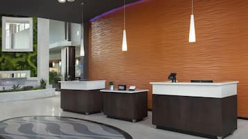 Zona de recepción de hotel con tres mostradores, diseño moderno y una alfombra grande y curvada.