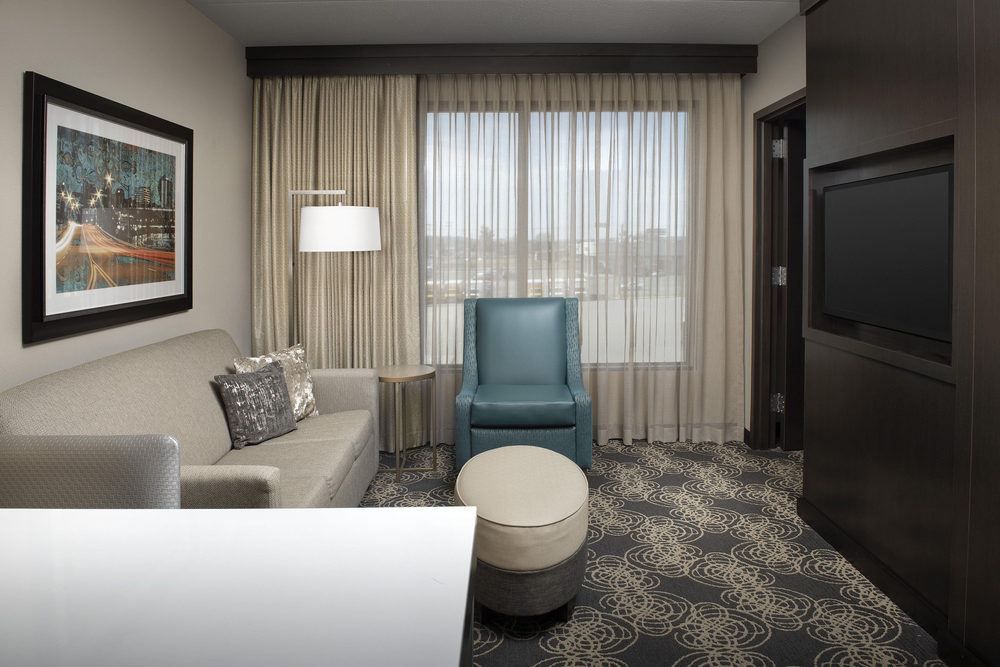 A hotel room with a sofa, a chair, a small round table, a television, and a window with curtains.