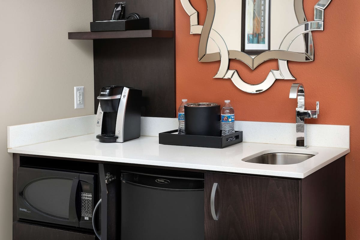A compact kitchen with a coffee maker, water bottles, a microwave, and a dishwasher.