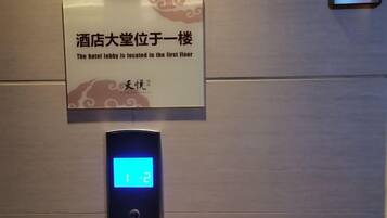 A digital elevator display with the number 12, a sign indicating the hotel lobby is on the first floor, and a metallic wall.
