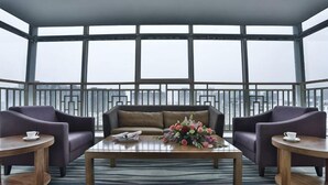 A modern lounge area with a sofa, two armchairs, a coffee table, and a view through large windows. - Tianyue Hotel (Chengdu)