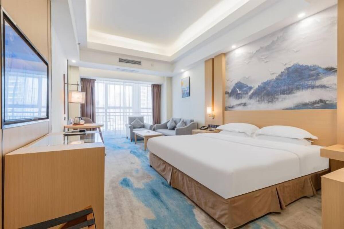 A hotel room with a large bed, a desk, a chair, a sofa, and a large painting on the wall.