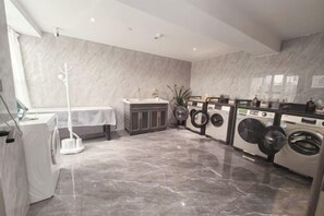 A modern laundry room with a marble floor, a washing machine, a dryer, and a drying rack. - Tianyue Hotel (Chengdu)