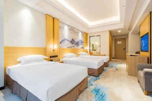Une chambre d’hôtel avec trois lits, un grand tableau au mur, une télévision et un bureau.