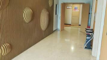 Een hotelgang met een houten wand met ronde patronen, een prullenbak en een deur met een bordje.