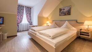 A bedroom with a bed, bedside tables, a TV, a window with curtains, and a painting on the wall. - Hotel AM Schlosspark (Ismaning)