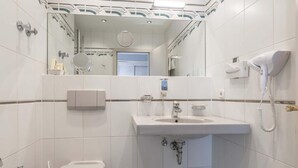 A bathroom with a sink, mirror, hairdryer, and towel dispenser. - Hotel AM Schlosspark (Ismaning)