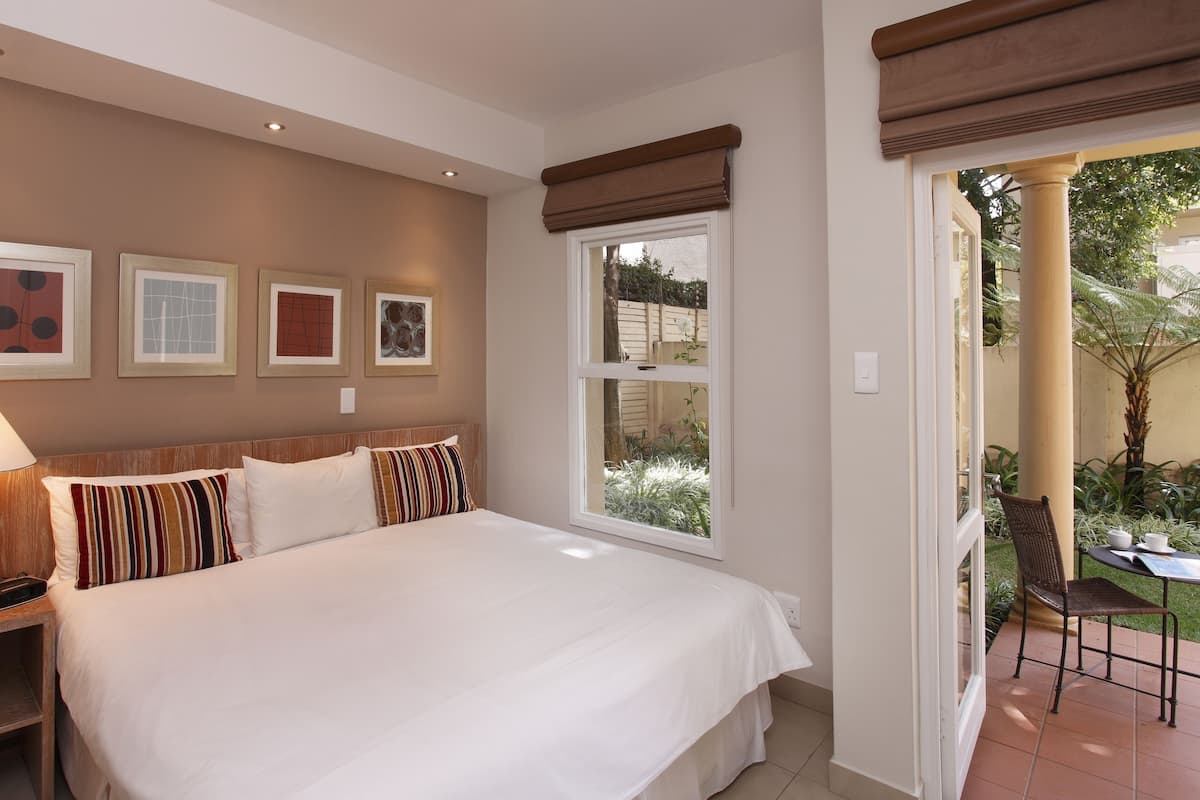 A hotel room with a large bed, a bedside table with a lamp, and a window with a view of the garden.