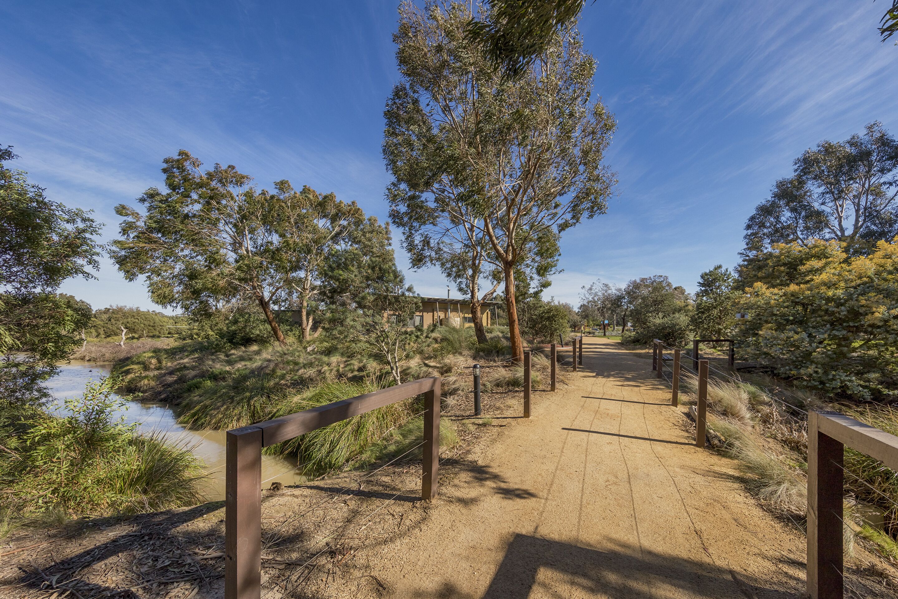A wooden boardwalk leading to a building with a clear view of a river and surrounding vegetation.