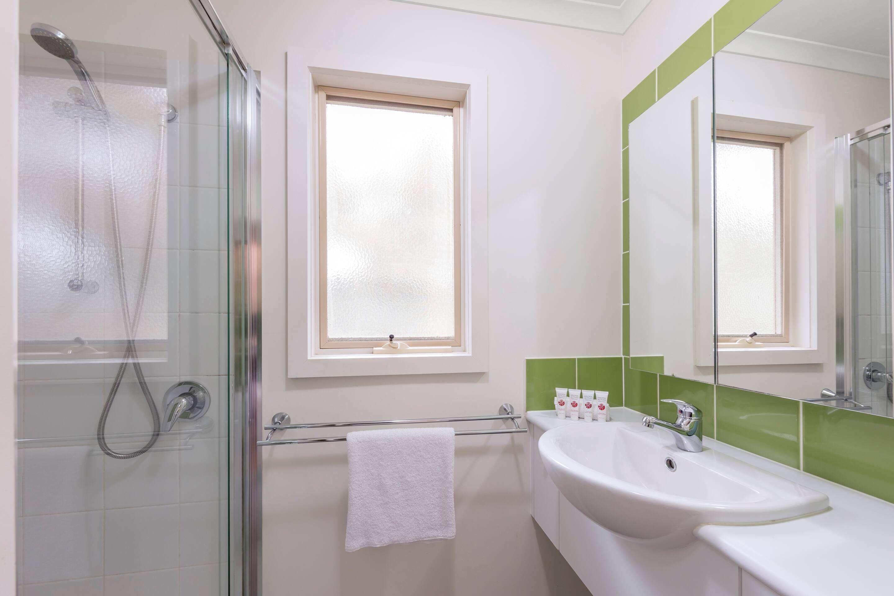 A bathroom with a glass shower enclosure, a white sink, a mirror, and a window.
