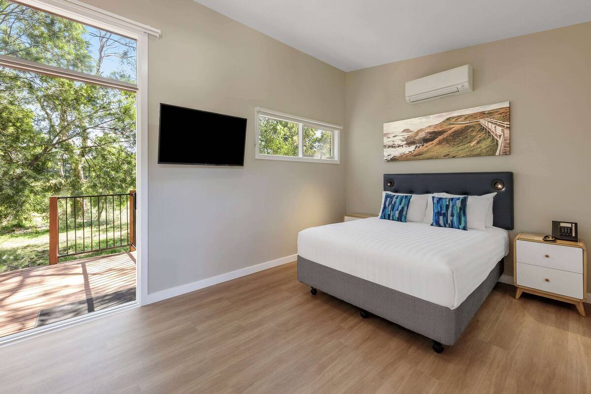 Ein Schlafzimmer mit einem Bett, einem Fernseher, einer Klimaanlage und einem Bild an der Wand.