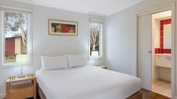 Un dormitorio con una cama, dos mesitas de noche, una ventana y una puerta que da a un baño.