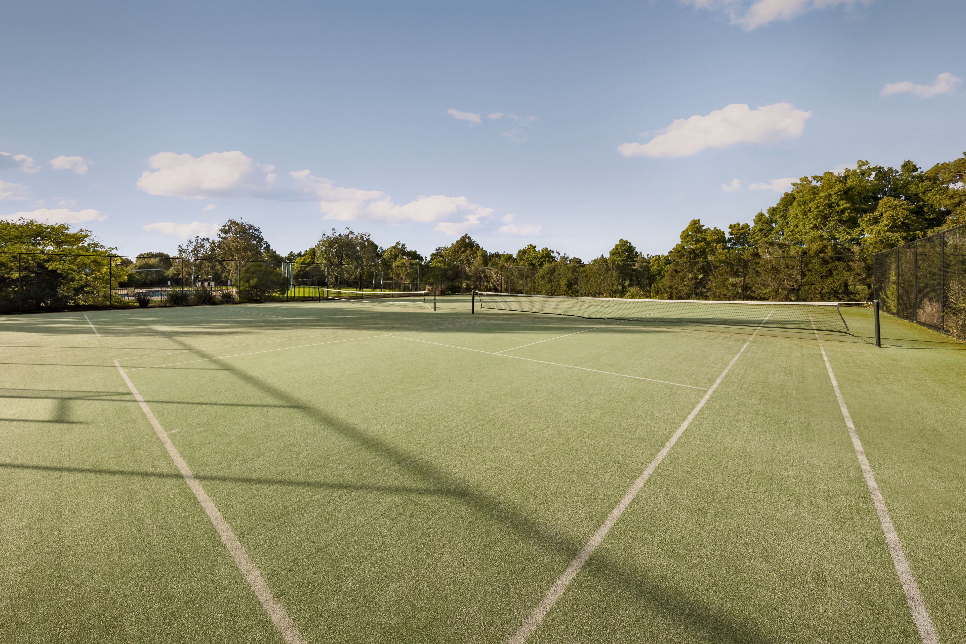 An outdoor tennis court with a net, surrounded by trees and a fence.