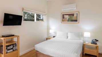 Une chambre d’hôtel comprenant un lit, des tables de chevet, une télévision, un climatiseur, une fenêtre et un tableau encadré au mur.