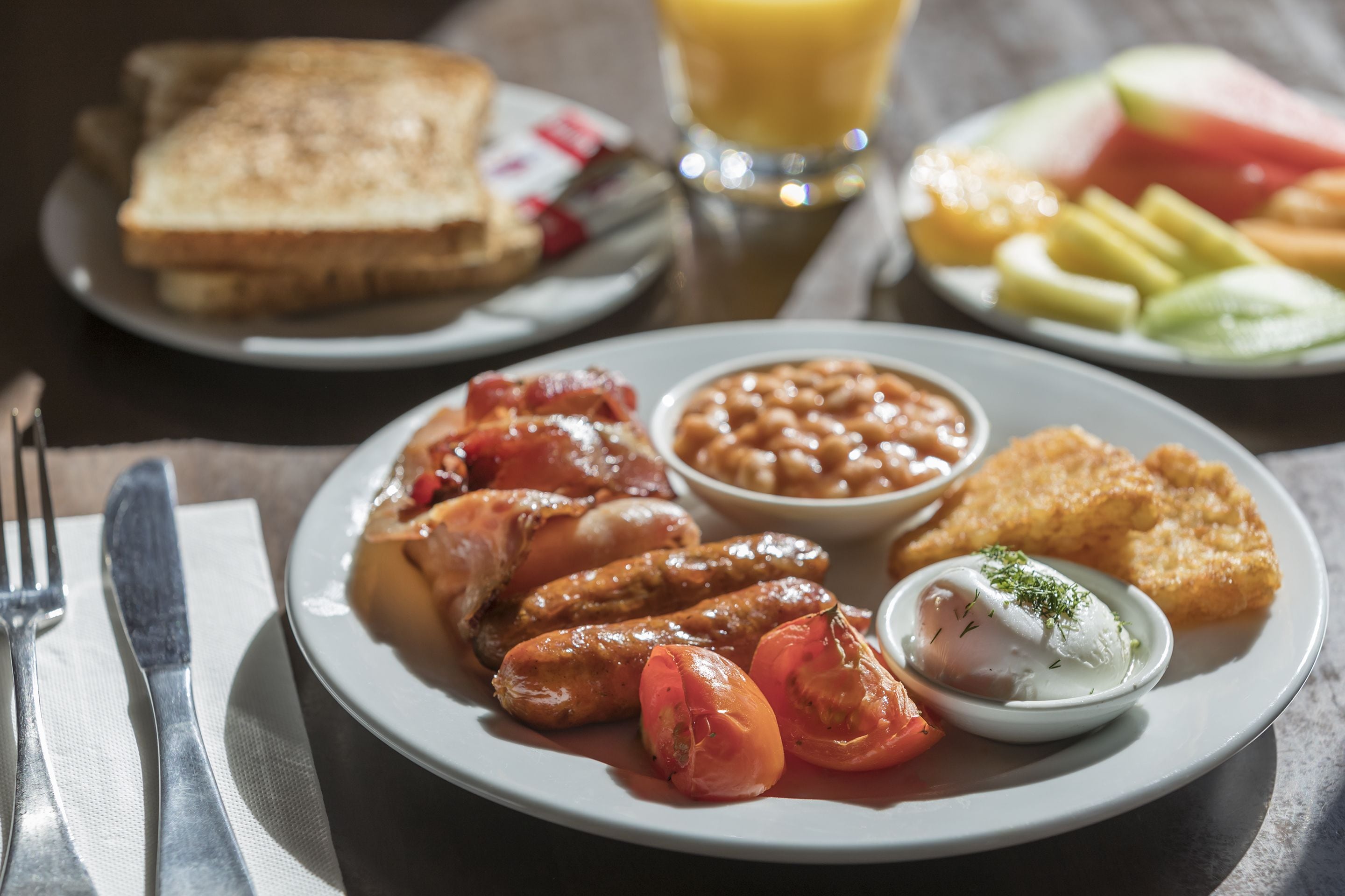 A breakfast plate with sausages, tomatoes, beans, and a poached egg.