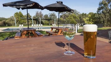 Ein Bierglas auf einem Holztisch, im Hintergrund Picknicktische und Sonnenschirme.