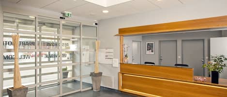 A reception area with a wooden reception desk, a glass door entrance, and a reception mat with the word "Reception" on it.