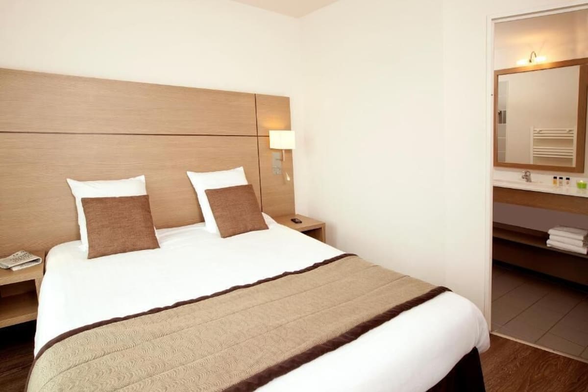 A hotel room with a large bed, a nightstand, a bedside lamp, a mirror, and a bathroom with a towel rack.