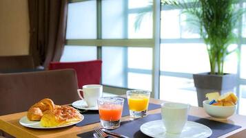 Una tavola imbandita per la colazione con croissant, succo d'arancia e una ciotola di frutta.