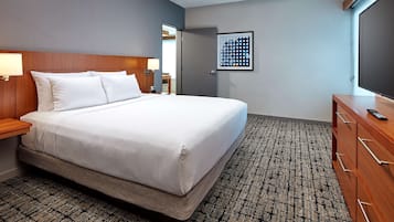 A hotel room with a large bed, wooden headboard, bedside table with lamp, a dresser, and a framed picture on the wall.