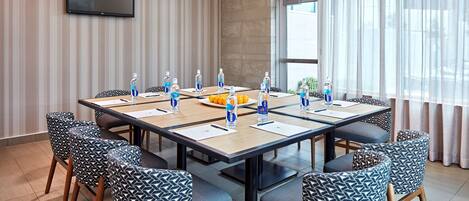 A conference room with a long table, chairs, water bottles, and a TV on the wall.